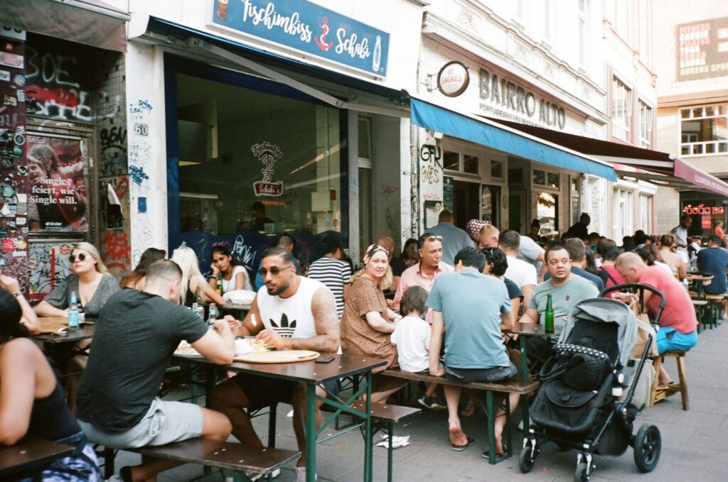 Lively outdoor cafe scene in urban setting with diverse group of people enjoying meals and socializing.