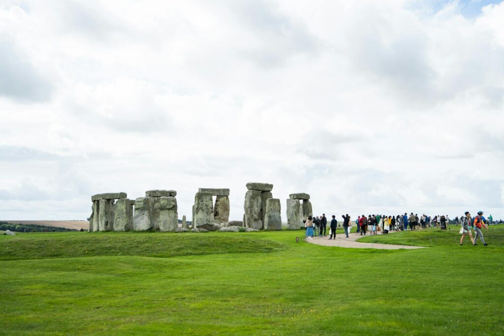 Tourists visit Stonehenge, under a cloudy sky, in England's green landscape.