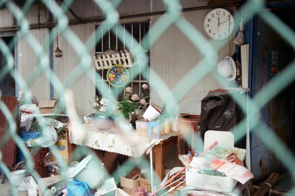 Cluttered room seen through a green chain-link fence.