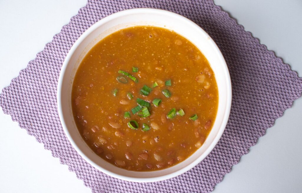 Hearty homemade bean soup garnished with green onions served in a white bowl.