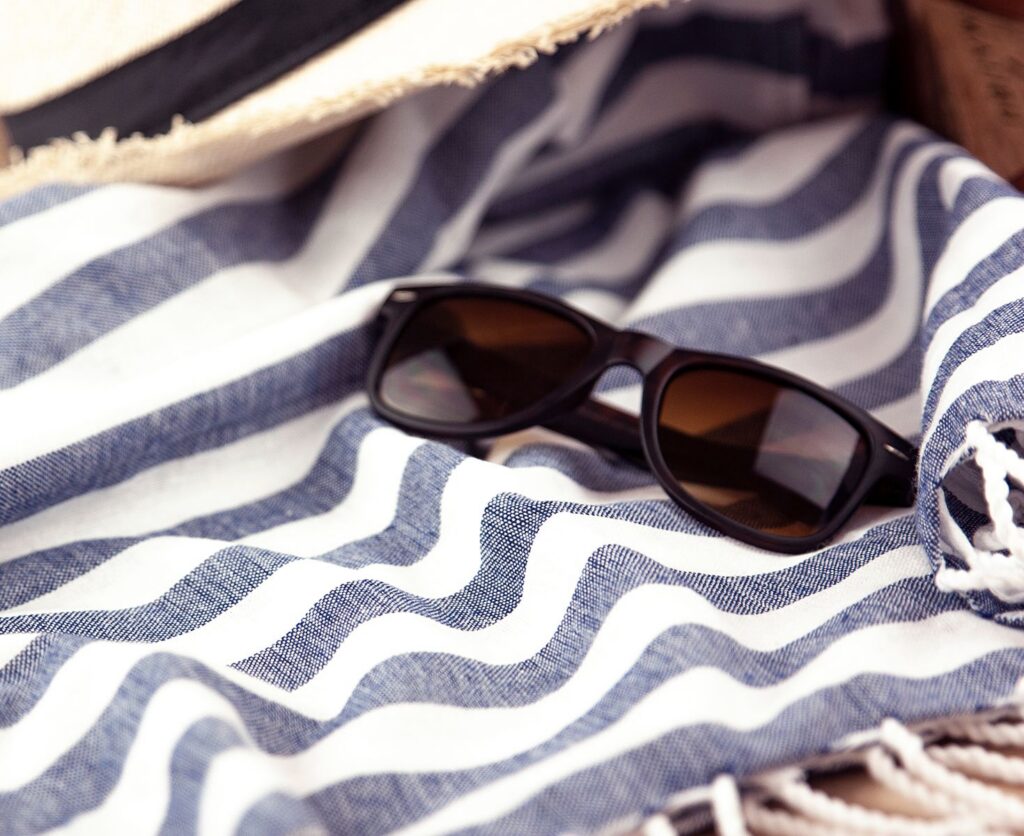 Close-up of stylish black sunglasses on a striped blue and white beach towel, perfect for summer leisure.