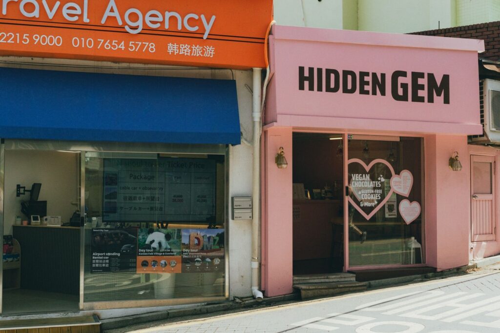 Explore the vibrant street shops of Seoul, featuring a travel agency and 'Hidden Gem' bakery.