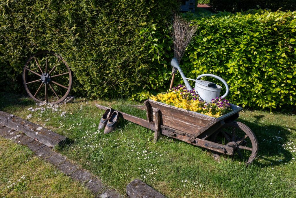 Charming garden setting features a vintage wheelbarrow filled with vibrant flowers, evoking a rustic countryside feel.