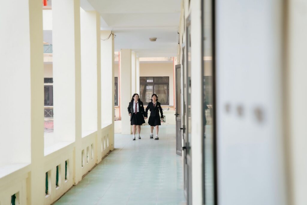 Two students in uniform walk through a bright school corridor.