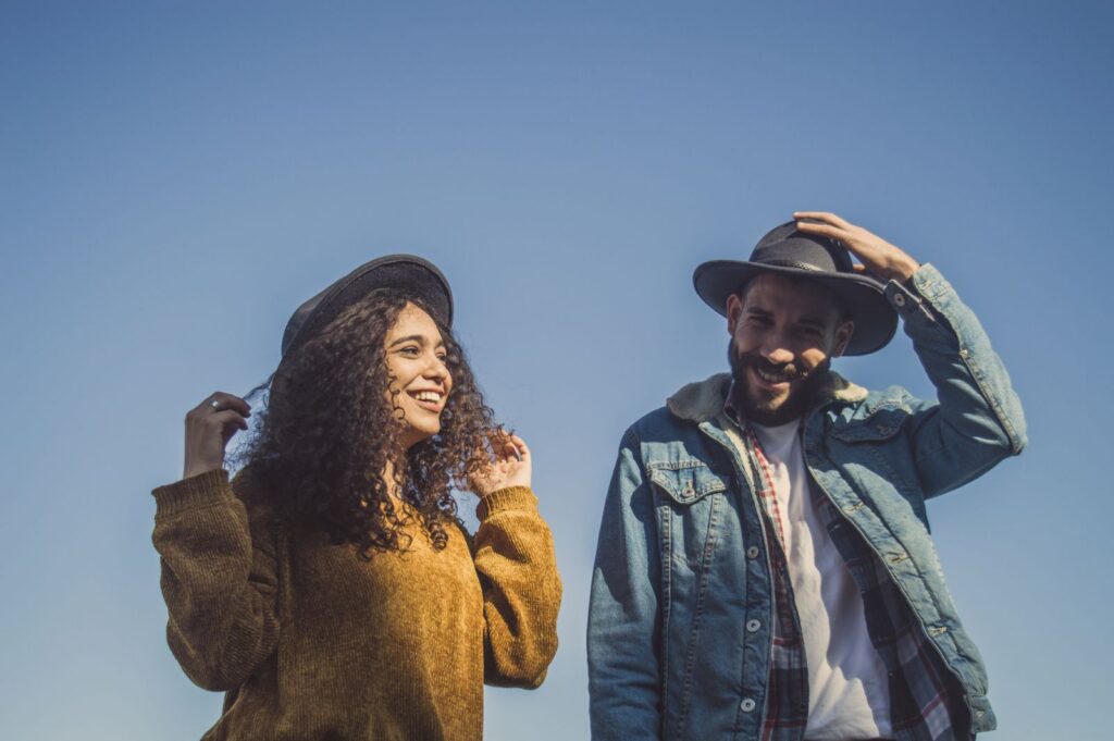 A joyful couple enjoying a sunny day, wearing stylish hats and casual outfits in an outdoor setting.