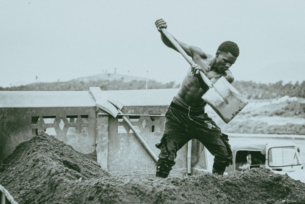 Young man working hard shoveling sand outdoors. Action and effort depicted.