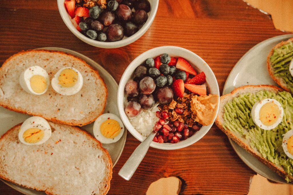 A fresh and vibrant breakfast flat lay featuring a yogurt bowl with fruits and toast with eggs and avocado.