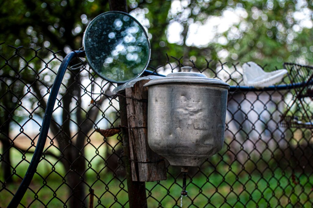 An outdoor water faucet on a wire fence with a mirror, offering a rustic rural aesthetic.