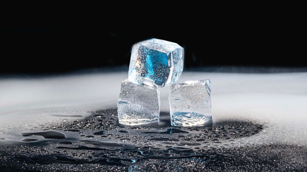 Three ice cubes melting on a black surface with water droplets.