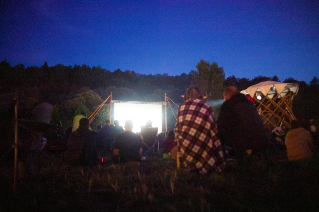 Adults gather outdoors for a night movie screening under the stars.