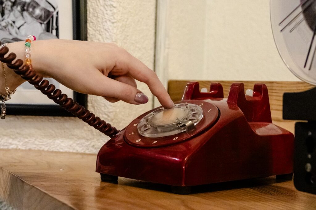 A close-up of a hand dialing a classic red rotary phone, capturing nostalgia.