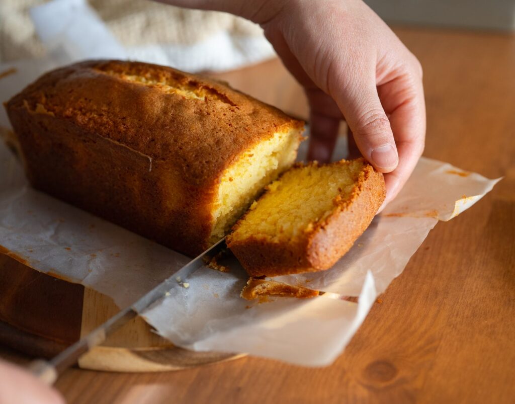 Close-up of a hand slicing a homemade pound cake, capturing the golden crust and soft texture.