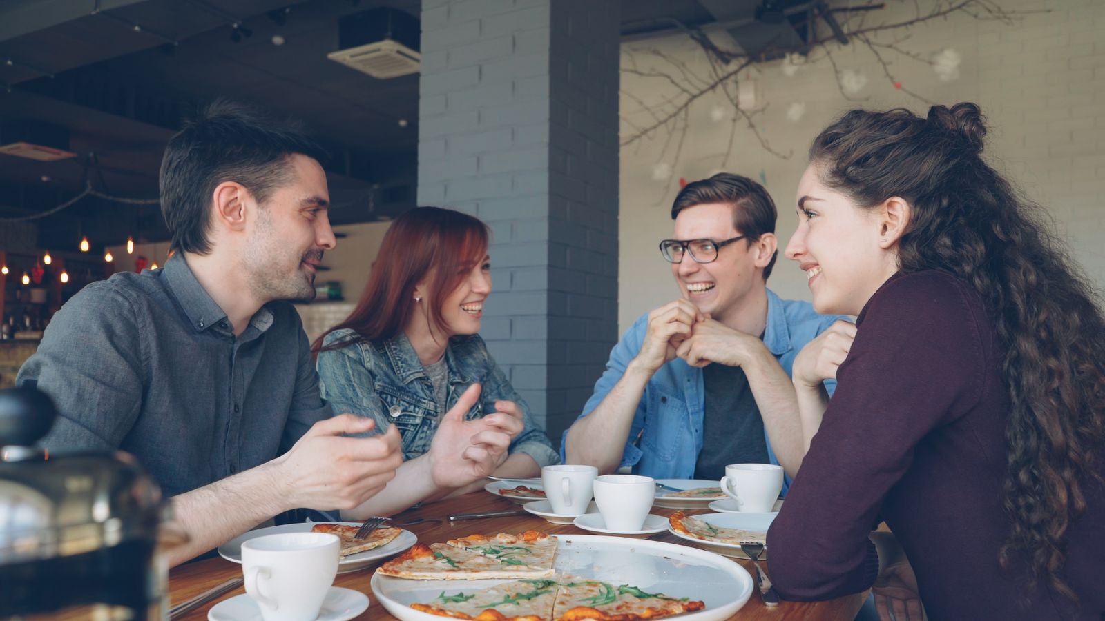 A group of friends having a fun conversation over pizza and coffee in a modern cafe, enjoying leisure time together.