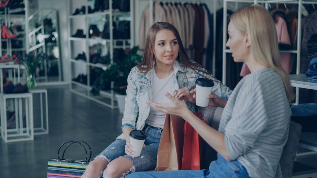 Two teens talking and enjoying coffee while shopping in a stylish boutique.