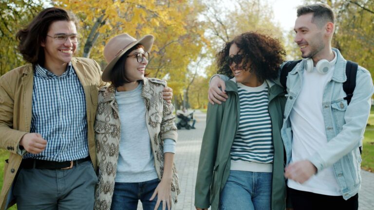 Group of friends laughing and walking in a park on an autumn day.