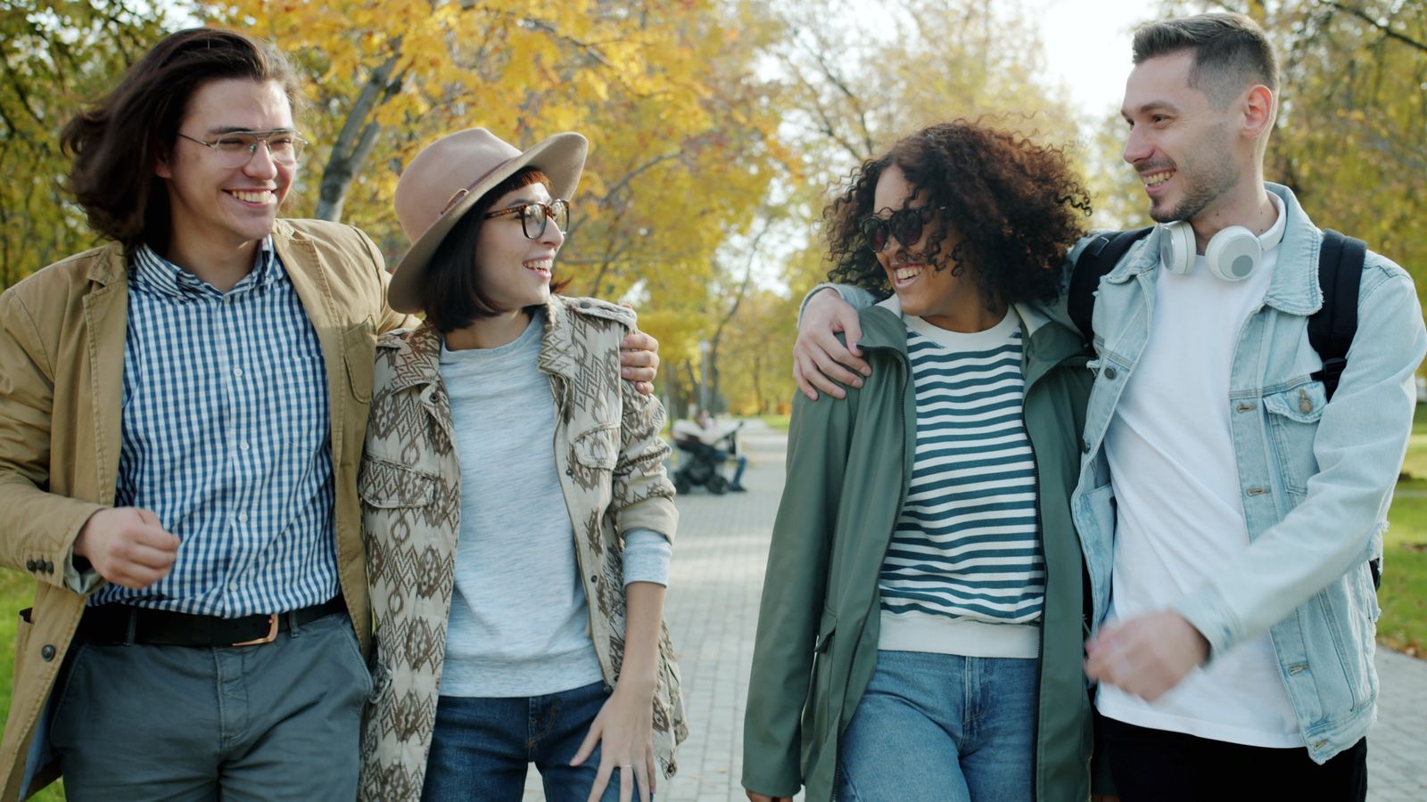 Group of friends laughing and walking in a park on an autumn day.