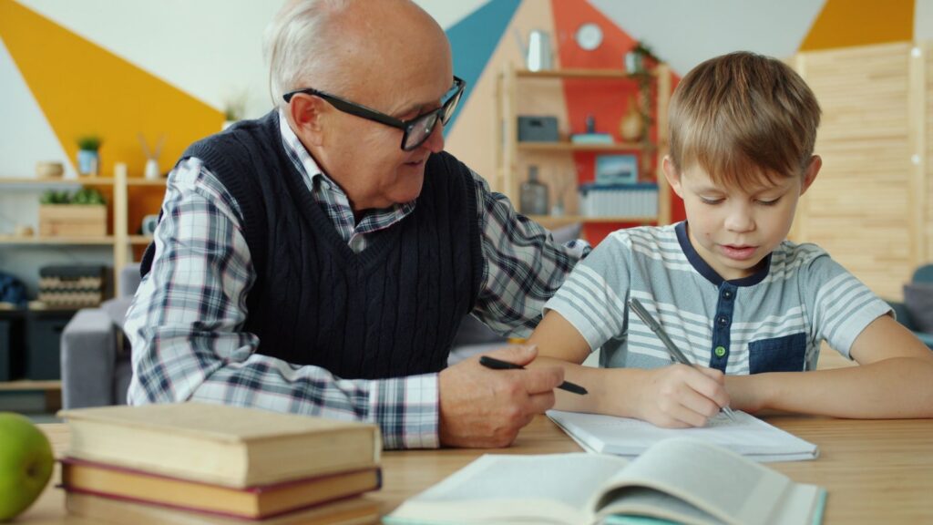 Senior man assisting young boy with schoolwork indoors, fostering learning.