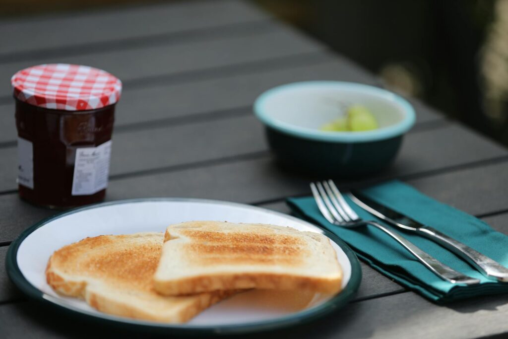 A cozy outdoor brunch setup featuring toast with jam, green grapes, and silverware on a table.