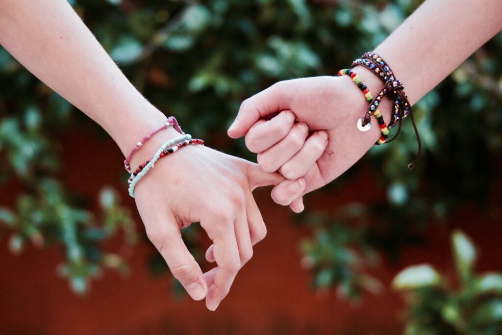 Two hands with colorful friendship bracelets interlocked, symbolizing friendship and connection.