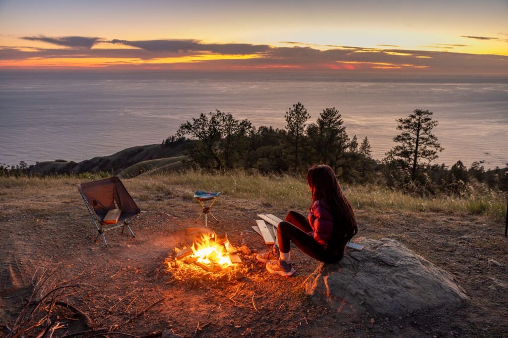 A person enjoys a campfire at sunset overlooking a stunning seascape. Perfect for outdoor and travel themes.