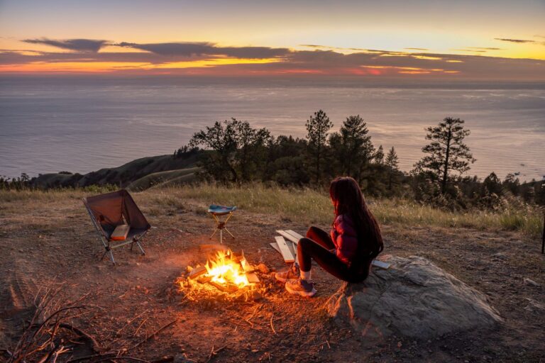 A person enjoys a campfire at sunset overlooking a stunning seascape. Perfect for outdoor and travel themes.