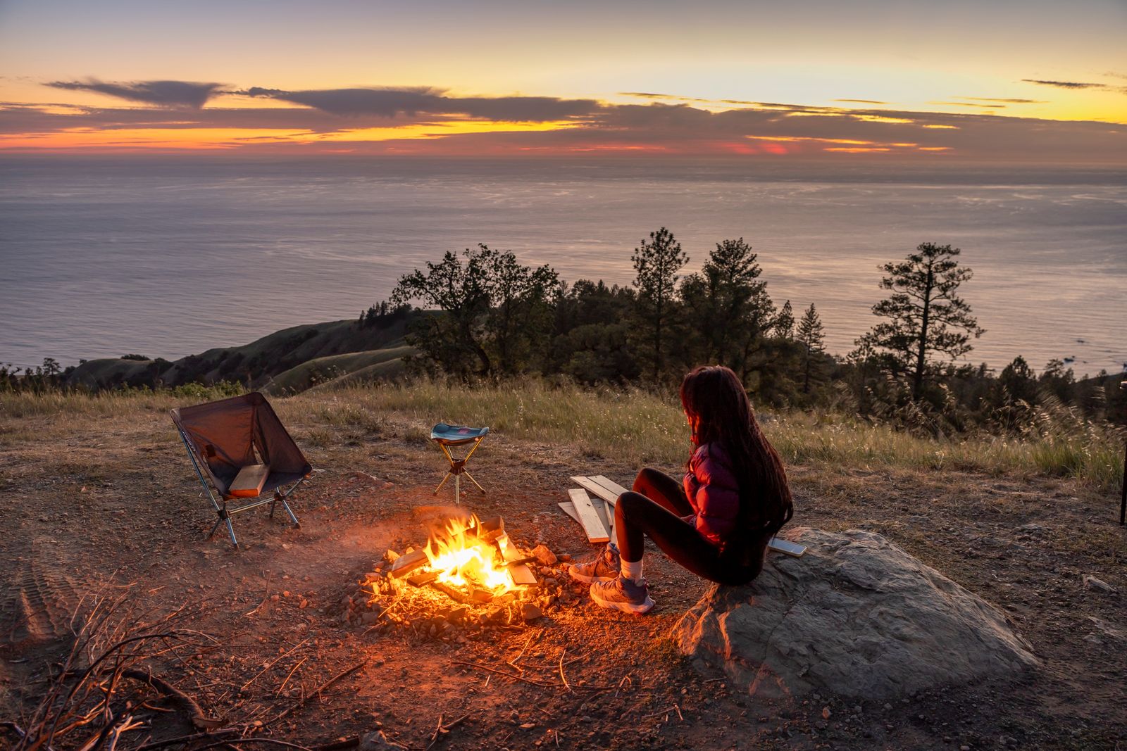 A person enjoys a campfire at sunset overlooking a stunning seascape. Perfect for outdoor and travel themes.