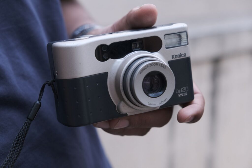 A hand holding a classic Konica film camera, showcasing retro design and style.
