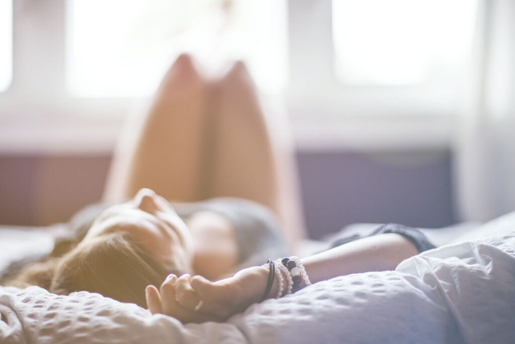 A woman lying on a bed in a peaceful, sunlit room, conveying relaxation.