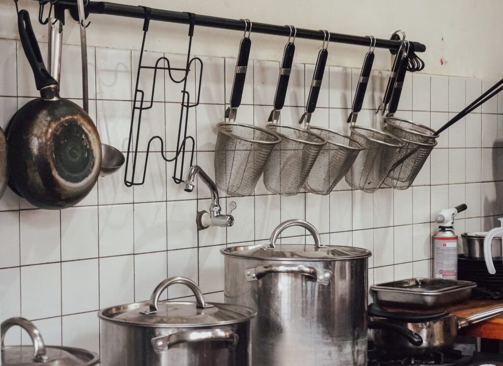 Industrial kitchen setup with hanging utensils and a row of cooking pots.