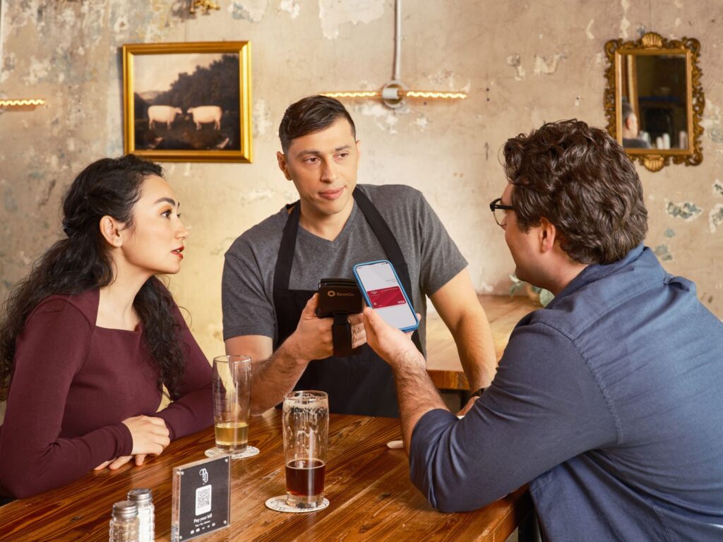 A couple makes a contactless payment using a smartphone at a restaurant bar counter.