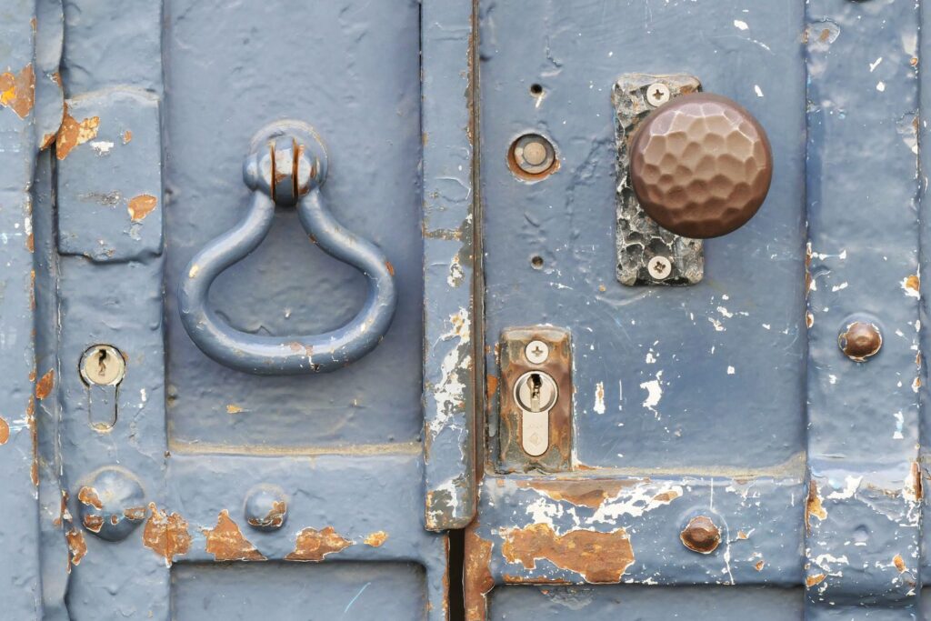 Close-up of a weathered blue door with a vintage knocker and rusty lock.