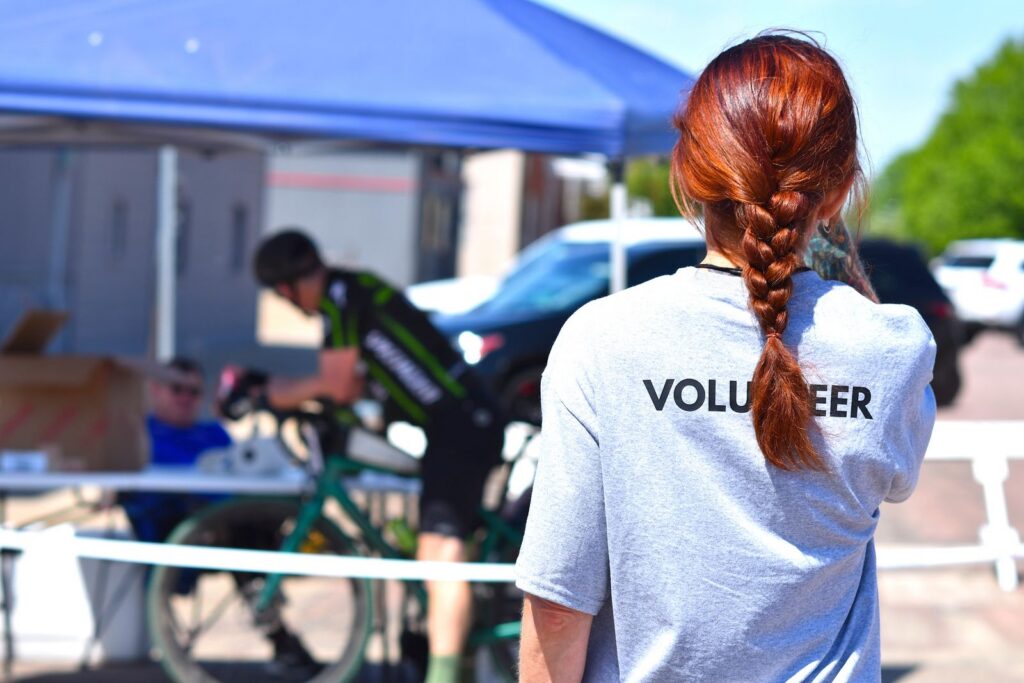 A volunteer oversees a charity bike event under a blue tent on a sunny day.