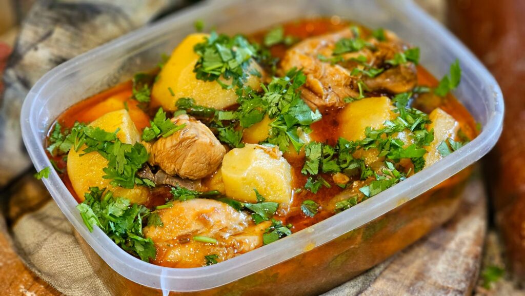 A mouth-watering chicken stew with potatoes and herbs in a transparent container.