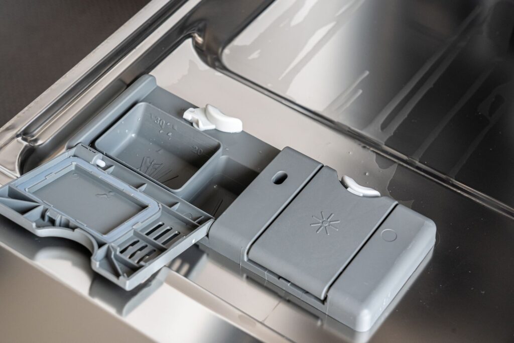 A detailed view of a dishwasher detergent compartment with soap residue.
