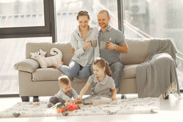 Cheerful family wearing casual clothes sitting in living room while playing and drinking tea during weekend at home in morning