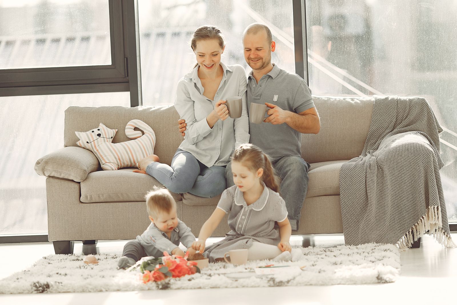 Cheerful family wearing casual clothes sitting in living room while playing and drinking tea during weekend at home in morning