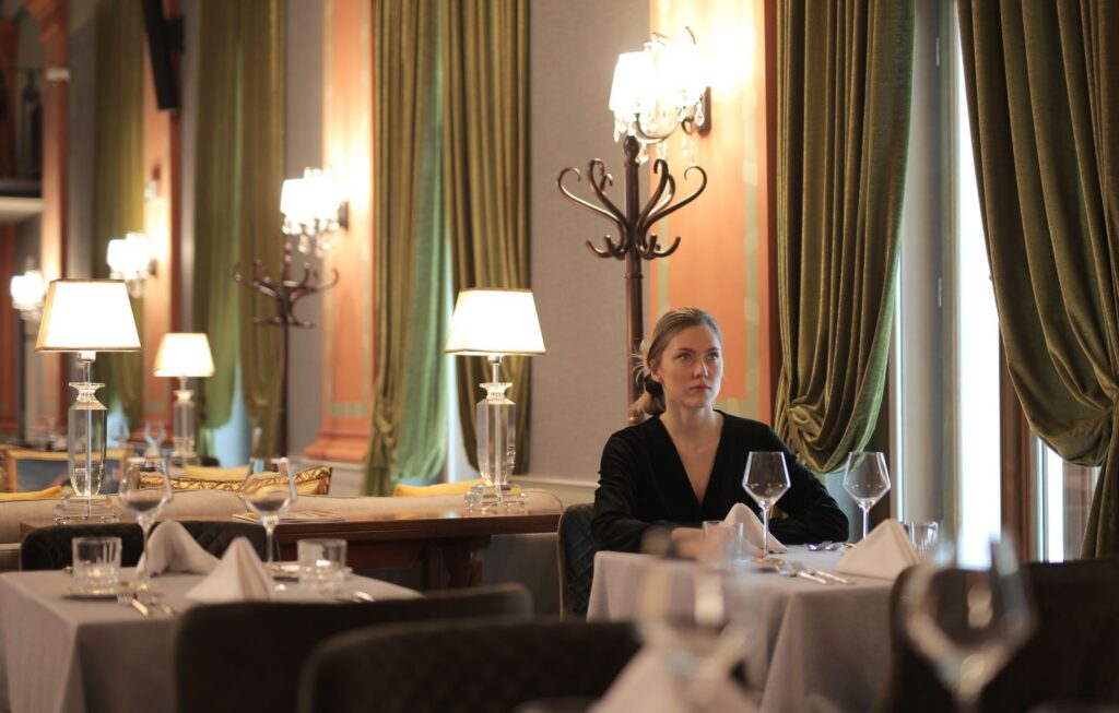 Woman sitting alone in a luxurious restaurant, surrounded by elegant decor and dim lighting.