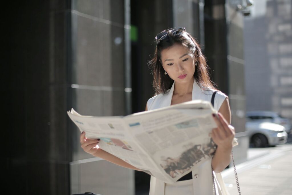 Stylish woman reading a newspaper on a sunny day in the city.