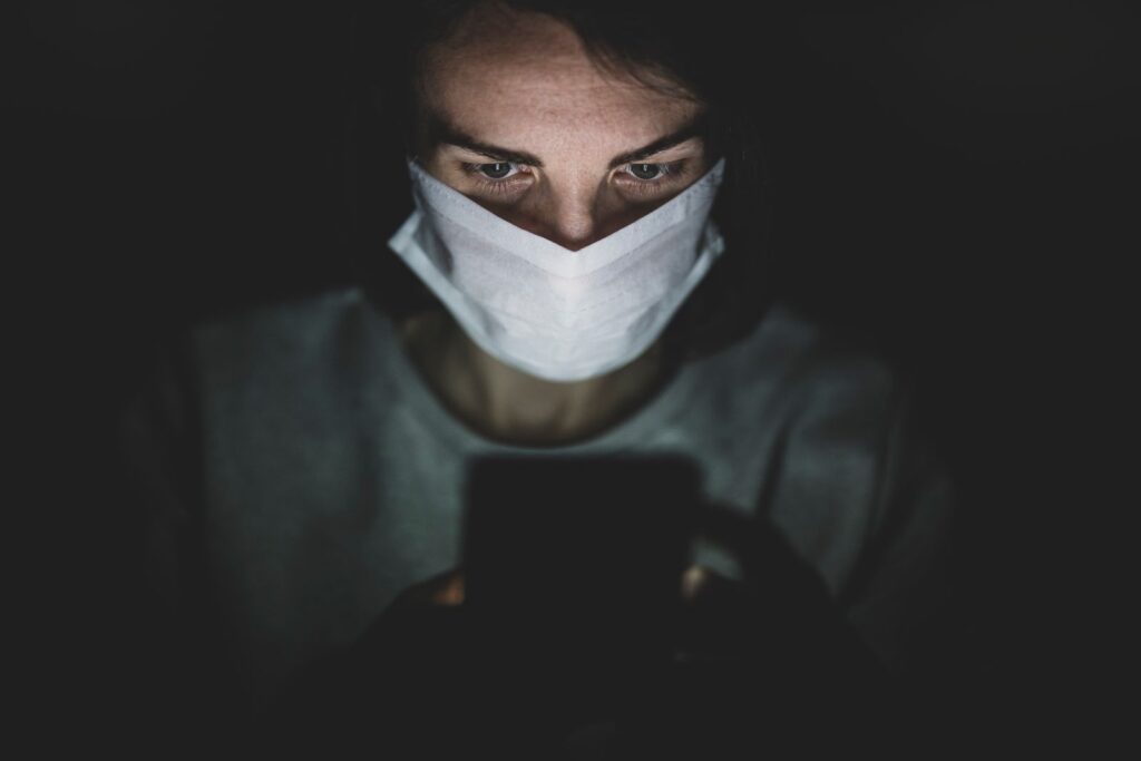 A focused individual wearing a mask uses a smartphone, highlighting the concept of isolation during a pandemic.