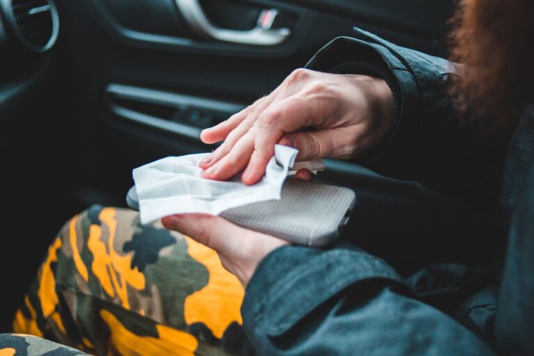 Faceless passenger in car disinfecting mobile phone with wet wipe sitting on car seat