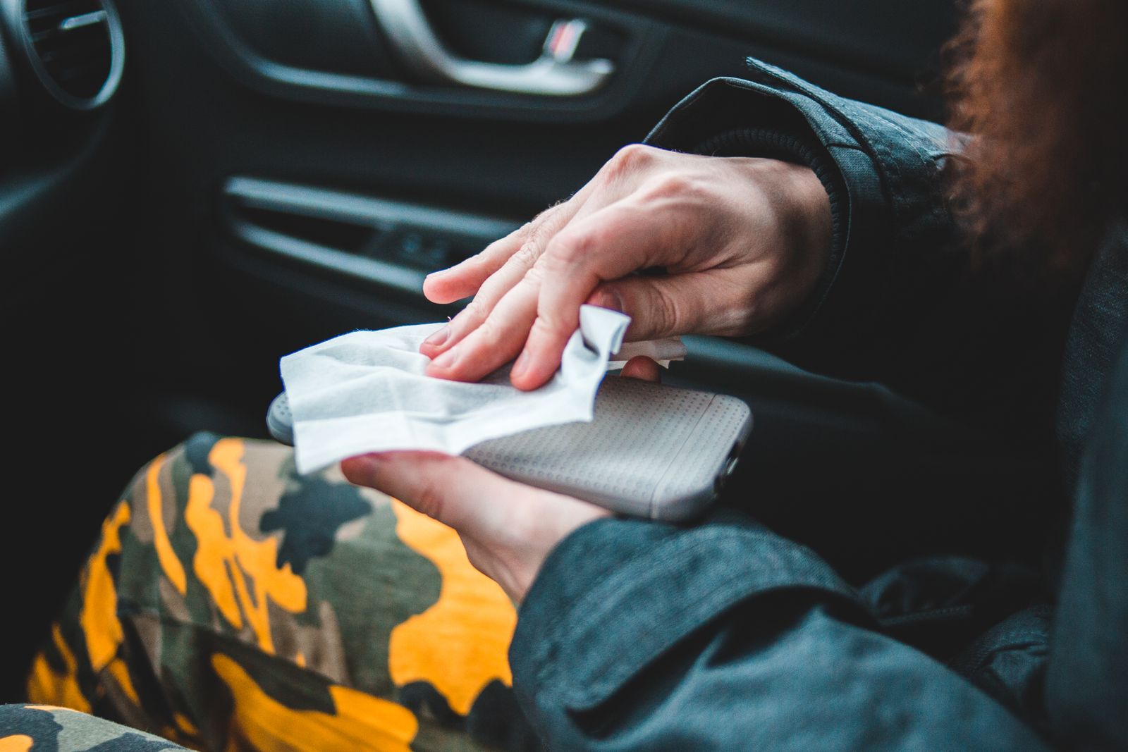 Faceless passenger in car disinfecting mobile phone with wet wipe sitting on car seat