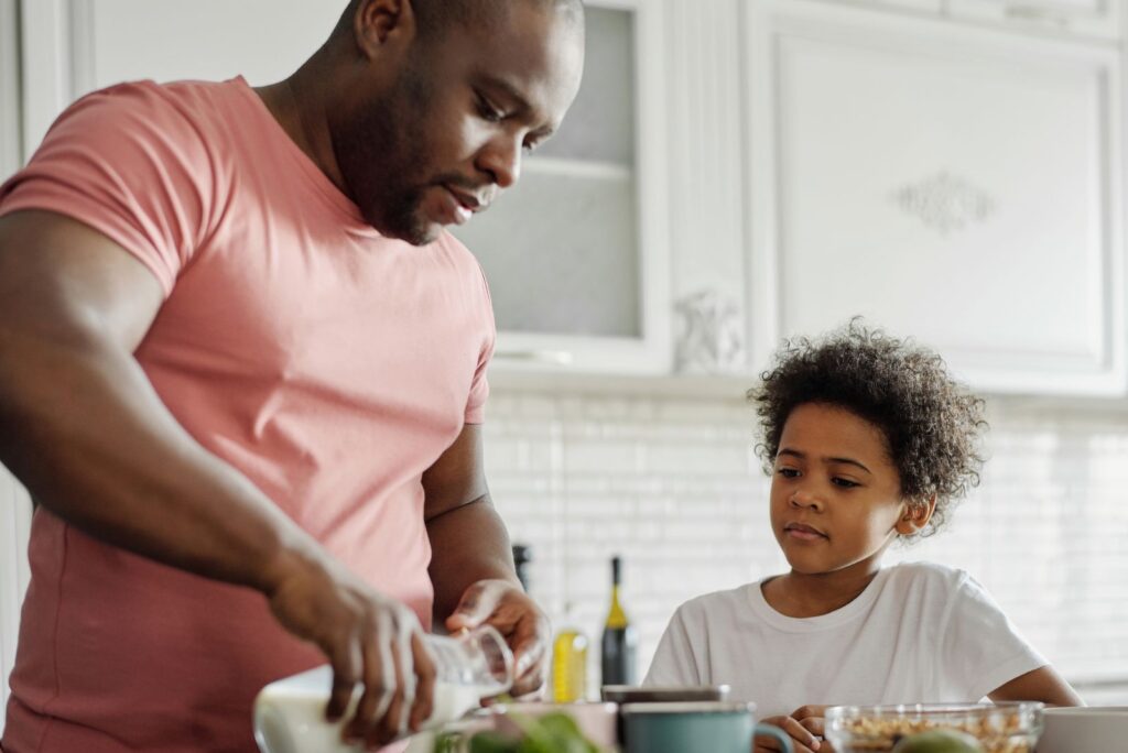 Father pouring milk with son watching in a cozy kitchen setting.