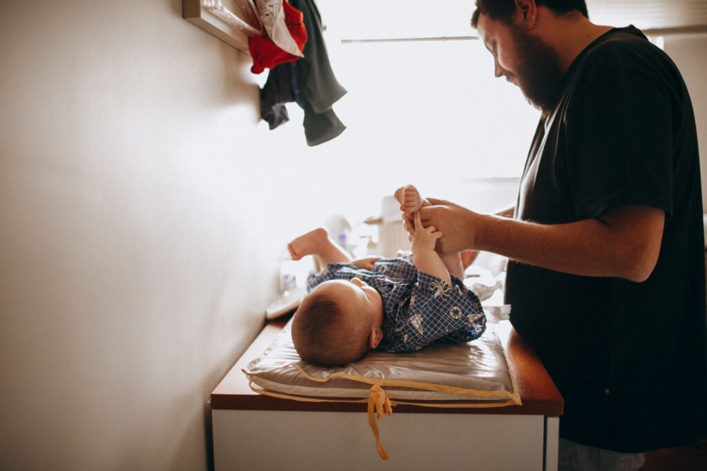 Happy dad in casual clothes standing near changing table and washing newly born son in morning time