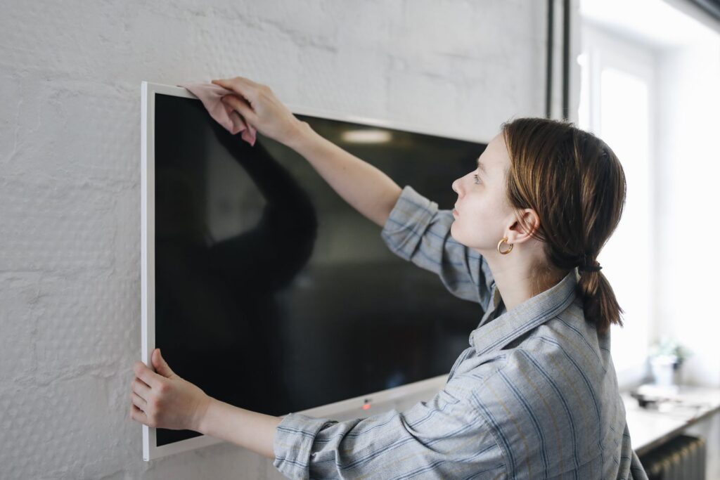 Woman wiping flat screen TV indoors, focusing on cleaning and maintenance.