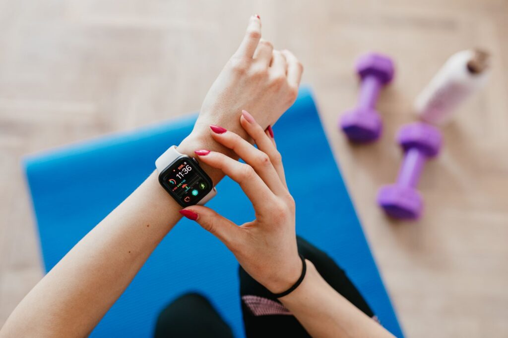 Unrecognizable female in sportswear sitting on blue yoga mat on floor and checking smart watch