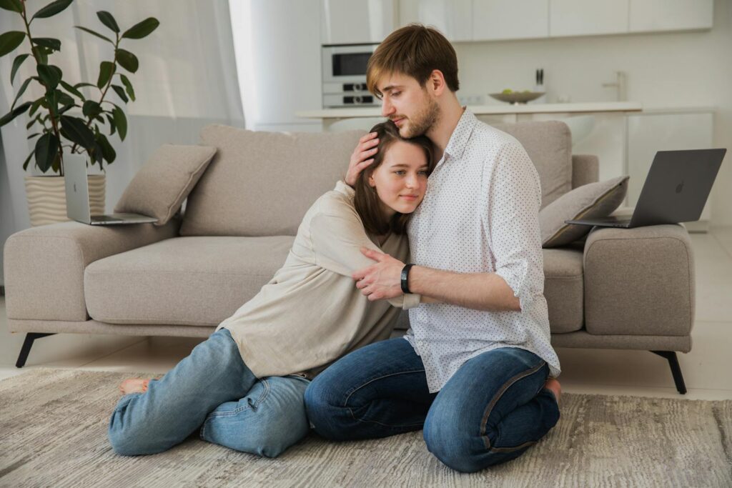 A tender moment between a young couple sitting on the floor in a modern living room.