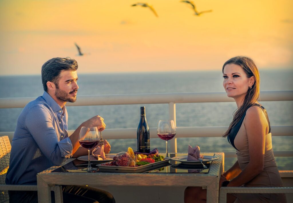 A couple enjoys a romantic dinner with wine at sunset overlooking the ocean.