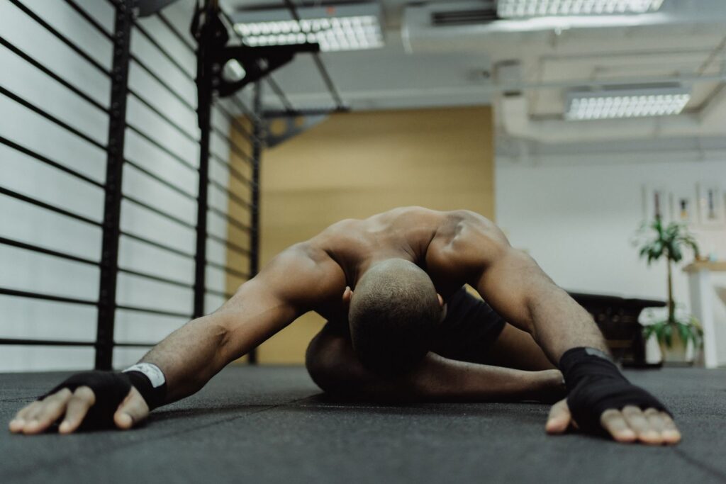 Shirtless man performing stretching exercise on gym floor, focusing on flexibility and strength.