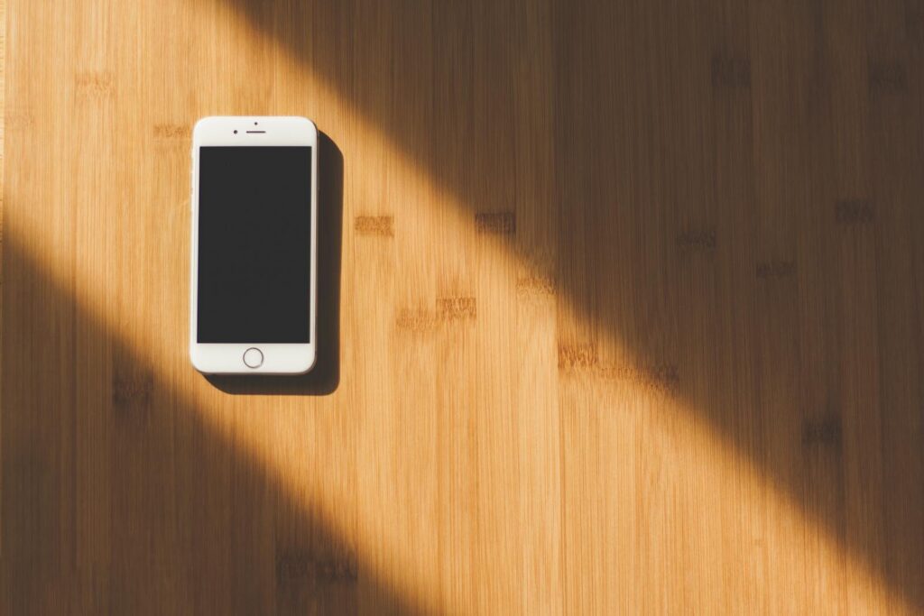 A sleek white smartphone lies on a sunlit wooden table, creating a minimalist tech aesthetic.