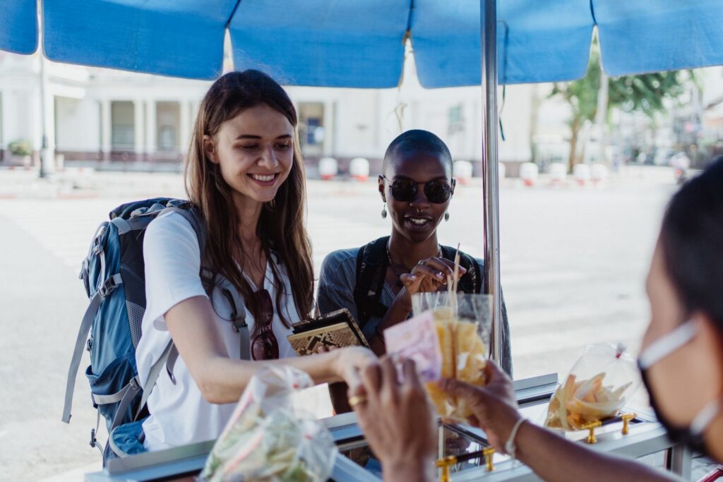 Travelers purchasing snacks from a street vendor at an outdoor market.